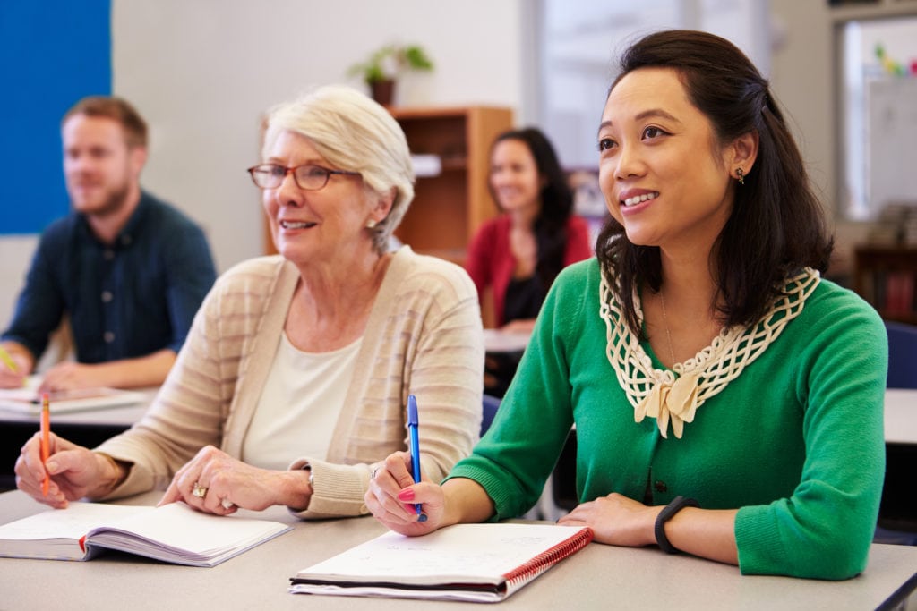 Two women sharing a desk at an adult education class look up in Glenolden PA Two women sharing a desk at an adult education class look up in Glenolden PA